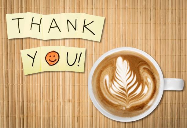 Coffee cup and thank you note on wooden background